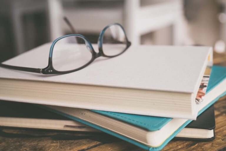 Eyeglasses on a stack of books in a cozy study setting, focusing on learning.