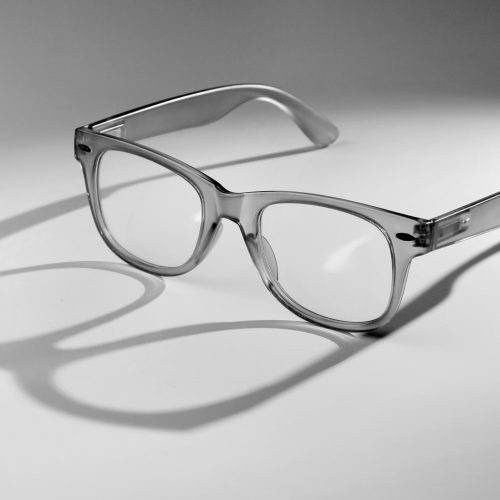 A pair of sleek, transparent eyeglasses casting shadows in a minimalist monochrome setting.