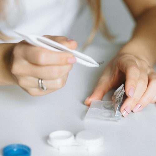 Close-up of a person using tweezers to handle contact lenses over a table.