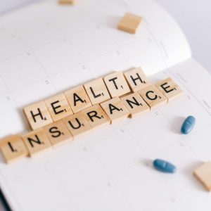 Close-up of health insurance spelled out with Scrabble tiles on a planner, alongside medication pills.
